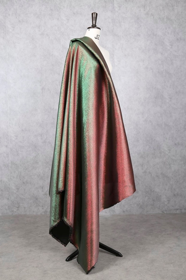 May include: A green and red iridescent fabric with a subtle shimmer. The fabric is draped over a dress form.