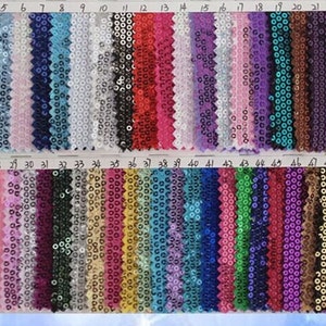 Op de afbeelding: Een kleurstaal met 50 verschillende kleuren van paillettenstof. De stof is gerangschikt in rijen van 10, waarbij elke rij genummerd is van 1 tot 50. De kleuren vari&euml;ren van licht tot donker en omvatten tinten van goud, zilver, rood, blauw, groen, paars, roze en zwart.