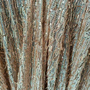 May include: A sheer fabric textile featuring a dense arrangement of rose gold sequins and thin, metallic rose gold bugle beads arranged in vertical, slightly irregular lines across a light-colored, fine mesh netting base material.