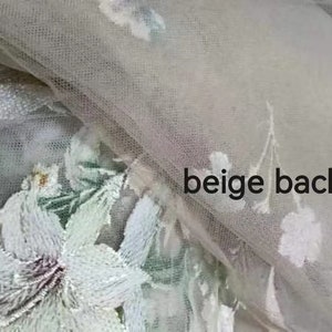 May include: White floral embroidery on a beige tulle fabric. The embroidery features delicate flowers and leaves.