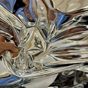 Könnte beinhalten: Silberner Metallic-Stoff mit einer zerknitterten, gekräuselten Textur. Der Stoff ist hochreflektierend und glänzend.