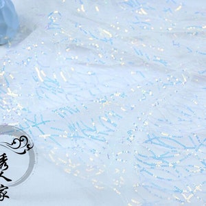 May include: Light blue iridescent sequins on a sheer mesh fabric. The sequins are arranged in a wavy pattern.