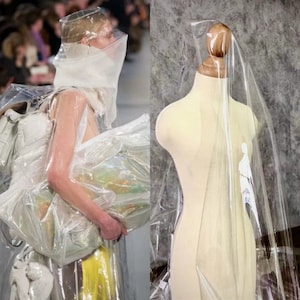 Puede incluir: Imagen de moda que presenta a una persona con un atuendo de plástico transparente y un maniquí cubierto con plástico transparente. La persona sostiene una gran bolsa de plástico transparente. El maniquí es beige con cuello de madera.