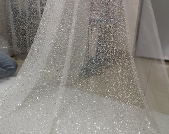 Könnte beinhalten: Weißer Tüllstoff mit glitzerndem silbernen Glitzerfinish. Der Stoff ist durchsichtig und hat eine zarte Textur.