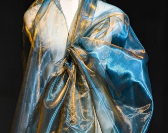 May include: A sheer, iridescent fabric wrap draped over a mannequin. The material features a dual-tone effect, shifting between a vibrant teal blue and a warm metallic gold depending on the light, with a crisp, semi-transparent organza texture.