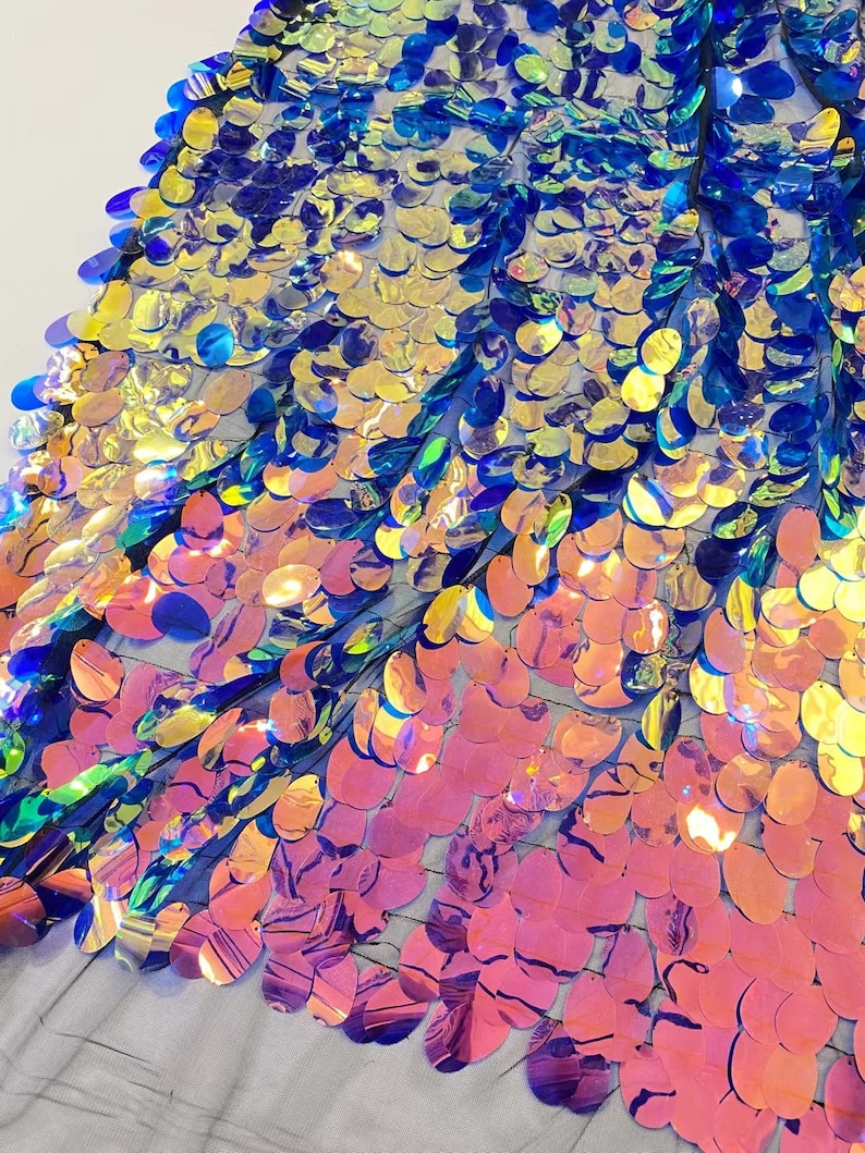 May include: Iridescent blue, gold, and pink oval sequins on a mesh fabric. The sequins are arranged in a graduated pattern, with the blue sequins at the top and the pink sequins at the bottom.