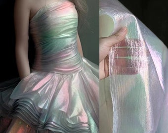 May include: A white iridescent fabric with a subtle rainbow sheen. The fabric is sheer and has a delicate texture. It is shown draped over a hand and also used to create a dress.