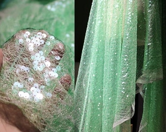 May include: Green mesh fabric with iridescent sequins. The fabric is sheer and has a delicate texture.