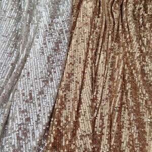 May include: Close-up of a fabric with two different colours of sequins. The left side is a light silver colour and the right side is a bronze colour.