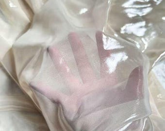 May include: A sheer, off-white fabric with a glossy, reflective finish. The material is lightweight and translucent, allowing the shape of a hand placed underneath to be clearly visible through the folds of the shimmering, smooth textile surface.
