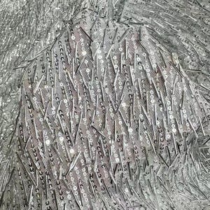 K&ouml;nnte beinhalten: Silberner Stoff mit einer strukturierten, glitzernden Oberfl&auml;che. Der Stoff ist mit kleinen, silbernen Pailletten bedeckt und hat einen fransigen Look.