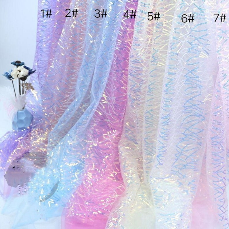 May include: Seven swatches of iridescent fabric with a light blue, pink, and white color gradient. The fabric has a delicate, sparkly texture and a subtle pattern of small, wavy lines.