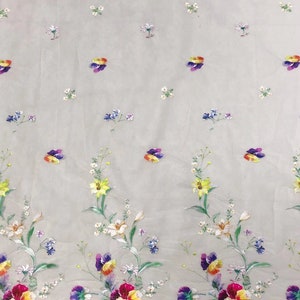 May include: White sheer fabric with a floral pattern. The flowers are yellow, purple, blue, and white. The fabric has a delicate, airy feel.