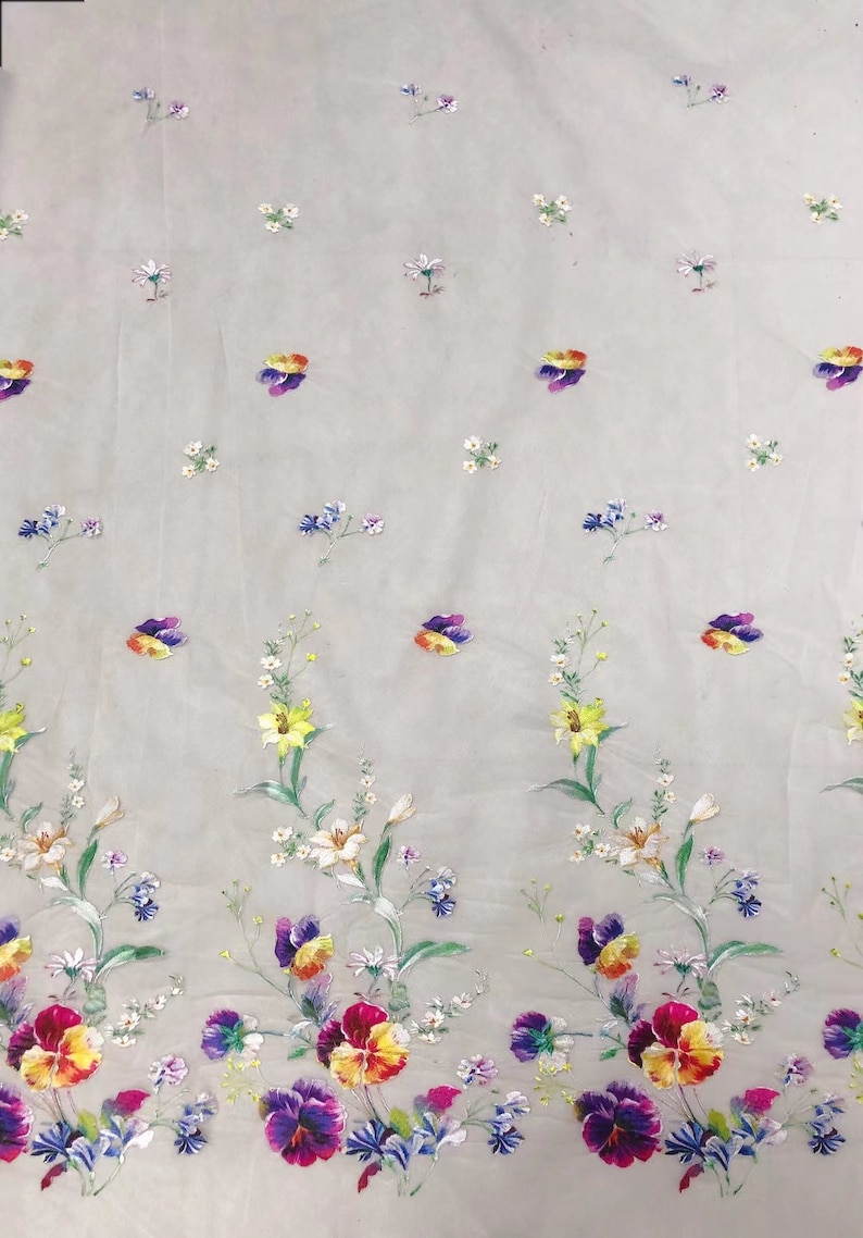 May include: White sheer fabric with a floral pattern. The flowers are yellow, purple, blue, and white. The fabric has a delicate, airy feel.