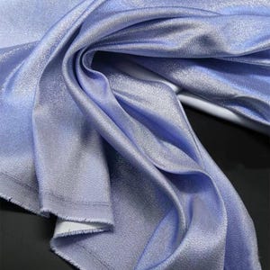 May include: A close-up of a light blue fabric with a subtle shimmer. The fabric is folded and draped, showcasing its soft texture.