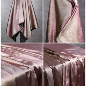 May include: A close-up of a metallic pink and gold fabric with a subtle shimmer. The fabric is draped and folded to show its texture and drape.