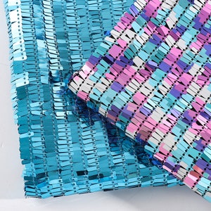 Puede incluir: Dos piezas de tela con un patrón de rayas azules y multicolores. Ambas telas están cubiertas de pequeñas lentejuelas rectangulares.