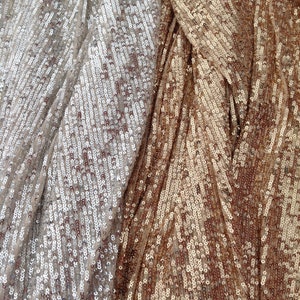 May include: Close-up of a fabric with a shimmering, iridescent finish. The fabric is made of sequins in two shades of gold, one lighter and one darker.