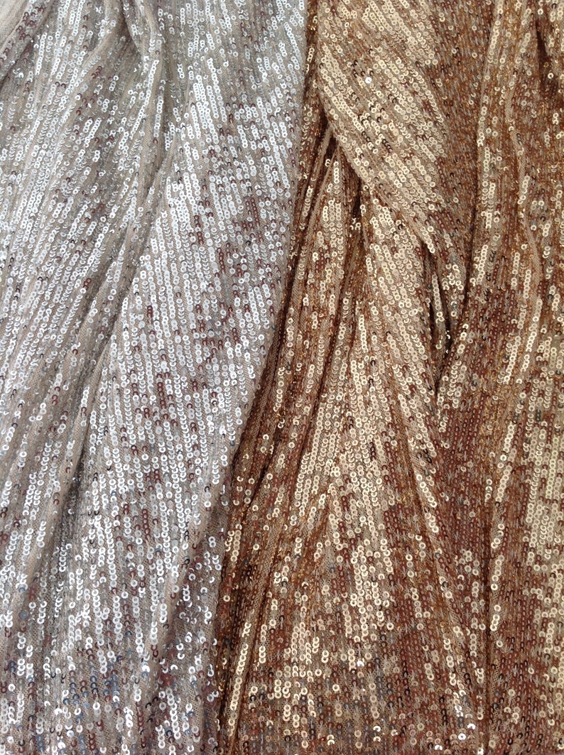 May include: Close-up of a fabric with a shimmering, iridescent finish. The fabric is made of sequins in two shades of gold, one lighter and one darker.