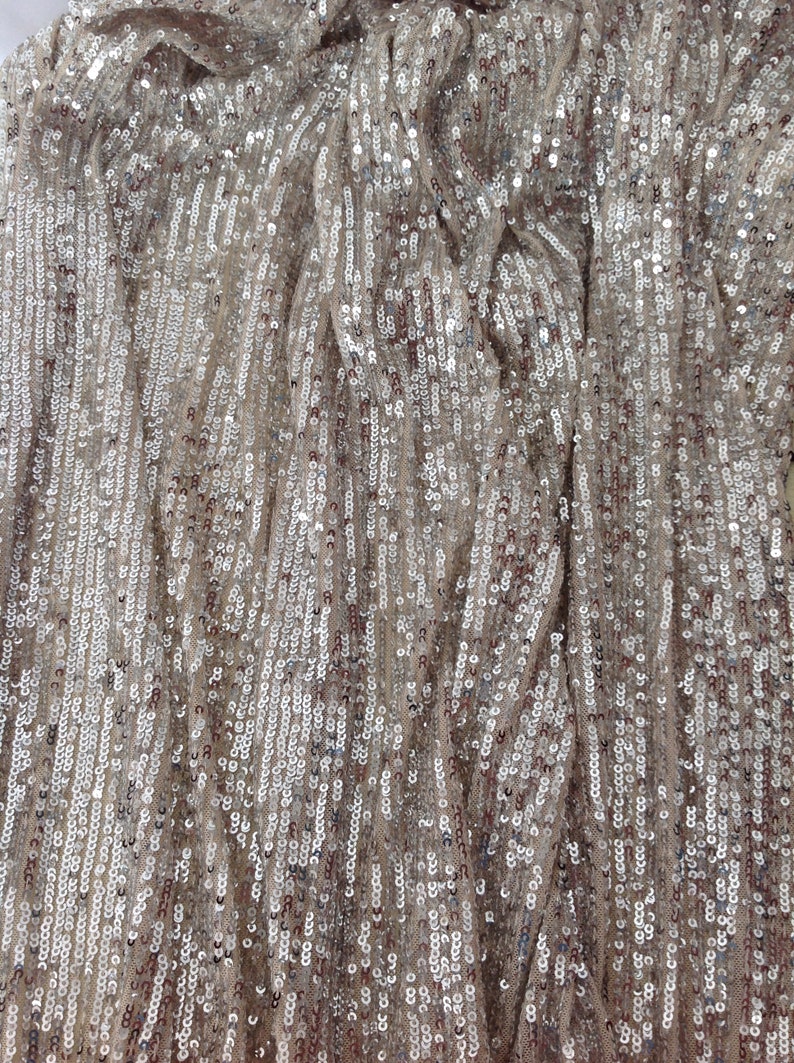 May include: Close-up of a fabric with a silver and beige sequin pattern. The sequins are arranged in vertical rows, creating a shimmering effect.