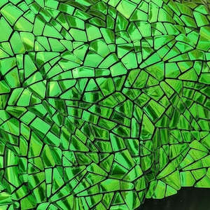 May include: Close-up of a shiny, green, mosaic-like fabric. The surface is made up of irregular, geometric shapes with a reflective, metallic finish. The shapes are outlined with black stitching, creating a textured appearance. The fabric has a dark, black background.