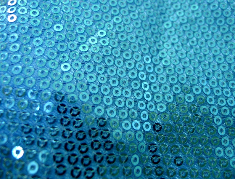 Op de afbeelding: Een close-up van een turquoise stof bedekt met pailletten. De pailletten zijn gerangschikt in een herhalend patroon.