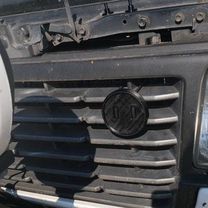 May include: A black car grille with a black circular emblem that says "01" in white lettering.
