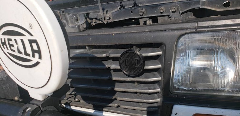 May include: A black car grille with a black circular emblem that says "01" in white lettering.