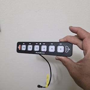 May include: A black remote control with six buttons and the text "AUXBEAM" and "MODE" printed on it. The remote has a black wire attached to it.