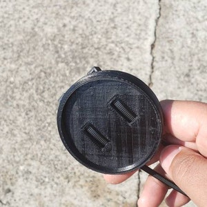 May include: Black plastic camera lens cap with two small rectangular openings.