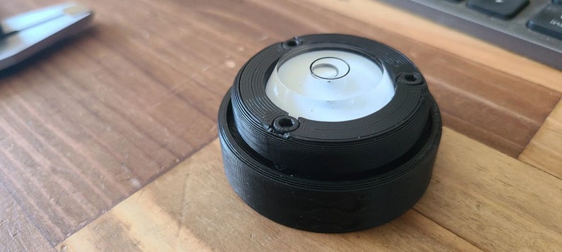 Puede incluir: Un nivel circular negro con un nivel de burbuja transparente en el centro. El nivel est&aacute; hecho de pl&aacute;stico y tiene una superficie texturizada.