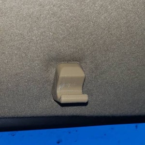 May include: A beige plastic hook attached to a gray car ceiling.