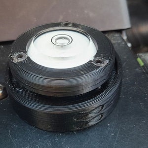Puede incluir: Un nivel circular negro con una ampolla de burbuja transparente. El nivel est&aacute; hecho de pl&aacute;stico y tiene una superficie texturizada.