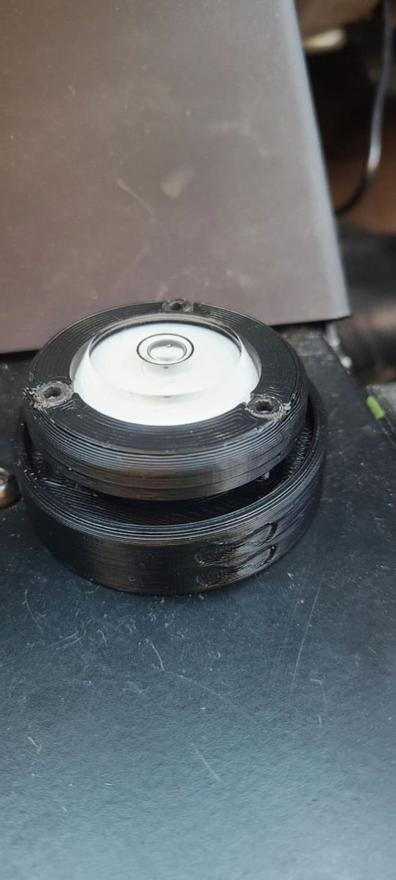 Puede incluir: Un nivel circular negro con una ampolla de burbuja transparente. El nivel est&aacute; hecho de pl&aacute;stico y tiene una superficie texturizada.