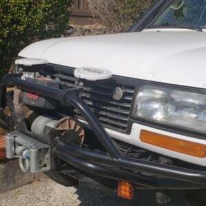 May include: White SUV with a black front bumper and a winch. The vehicle has two white antennas on the roof.
