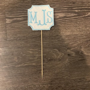 May include: White cake topper with blue trim and the letters "MJS" in blue.