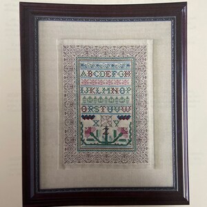 May include: A framed cross-stitch sampler featuring the alphabet, a floral design, and the text "Z is for Zinnia Sampler". The sampler is titled "Periwinkle Promises" by Barbara L. Rakosnik.