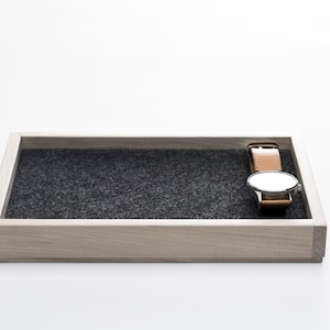 May include: A wooden tray with a gray felt lining and a silver watch with a brown leather band resting on the felt.