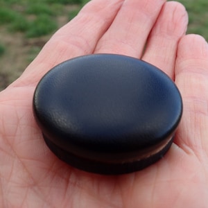 May include: A black round furniture leg cap with a smooth, slightly textured surface.