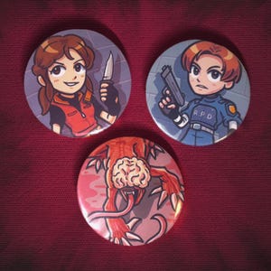 May include: Three round buttons with cartoon illustrations. One button features a woman holding a knife, another a man with a gun, and the third a monster with a brain. The buttons are set against a burgundy background.