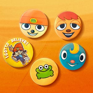 May include: Five colorful, round pinback buttons with cartoon character designs. The buttons feature various faces, a frog, and a character with the text "I GOTTA BELIEVE!". The buttons are set against an orange background.