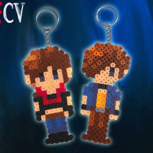 May include: Two pixel art keychains made from fused plastic beads. The left figure has brown hair, a red scarf, a black vest, and blue pants. The right figure has brown hair, a blue jacket, a yellow shirt, and brown pants. The text RECV is visible.