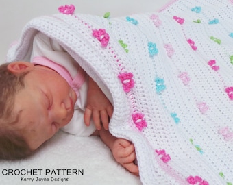 Könnte beinhalten: Eine weiße Häkeldecke für Babys mit einem Muster aus rosa, blauen und grünen Blumen. Die Decke ist aus weichem Garn gefertigt und hat eine zarte Textur. CROCHET PATTERN Kerry Jayne Designs