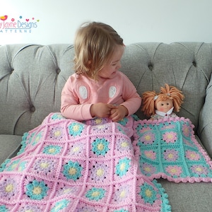 May include: A pink, blue, and yellow crocheted blanket with a matching doll blanket. The blankets feature a floral pattern and are next to a doll with orange hair. The image includes the text "Kerry Jayne Designs PATTERNS".