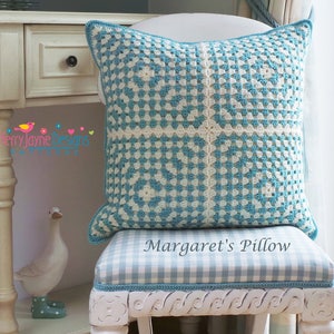 May include: A blue and white crocheted pillow with a square pattern. The pillow is sitting on a white chair with a blue and white checkered cushion. The text "Margaret's Pillow" is printed on the cushion.