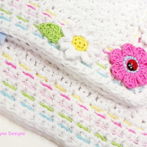 May include: White crochet baby blanket with a colorful striped border and flower appliques. The blanket features a pink flower with a ladybug button in the center. The label "Kerry Jayne Designs" is visible in the top left corner.