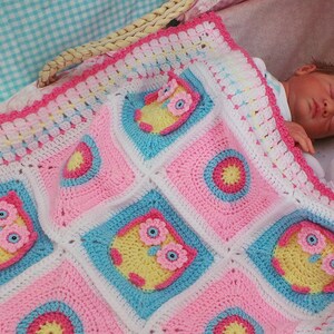 May include: A pink, blue, and white crocheted baby blanket with a scalloped edge and owl designs. The blanket is in a wicker basket with a baby doll sleeping on top.