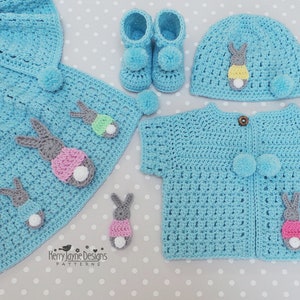 May include: A light blue crochet baby set featuring a blanket, booties, hat, and cardigan. Each item is adorned with gray, pink, yellow, and white bunny appliqu&eacute;s and pom-poms. The set is handmade and suitable for a baby.