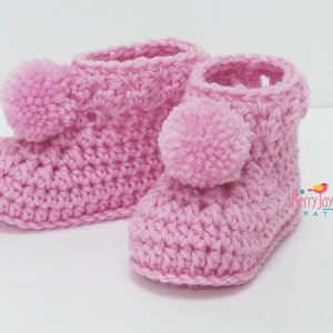 Puede incluir: Un par de botines de beb&eacute; de ganchillo rosa con pompones en la parte superior.