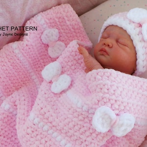 K&ouml;nnte beinhalten: Eine rosa geh&auml;kelte Babydecke mit wei&szlig;en geh&auml;kelten Blumen und einer passenden rosa-wei&szlig;en geh&auml;kelten M&uuml;tze.